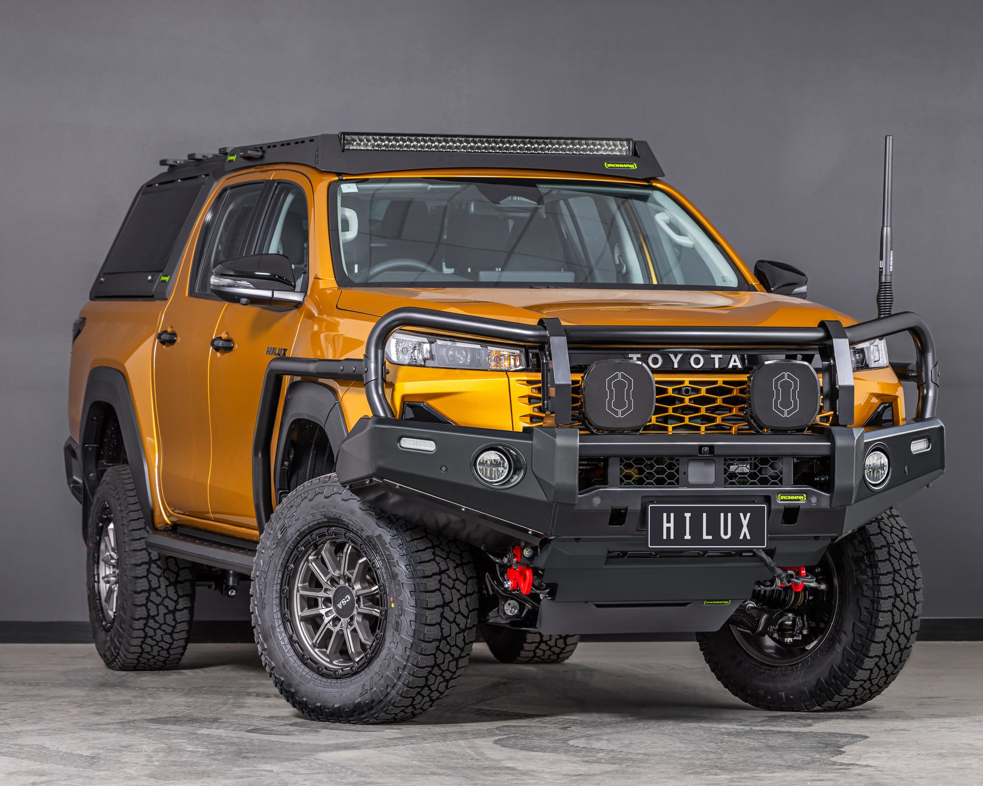 toyota hilux n90 2026 sunglow orange with ironman 4x4 deluxe bull bar front thee quarter angle also showing raid roof rack with integrated led light bar and raid canopy