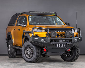 toyota hilux n90 2026 sunglow orange with ironman 4x4 deluxe bull bar front thee quarter angle also showing raid roof rack with integrated led light bar and raid canopy